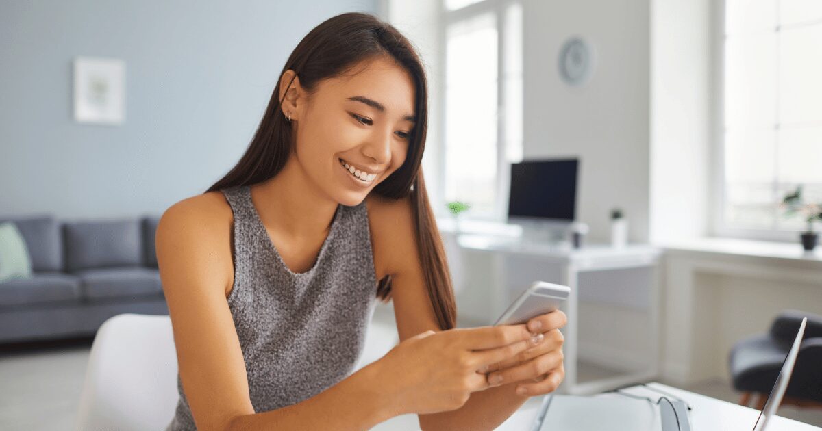スマートフォンを操作しながら笑顔を見せる女性。明るい室内でSNSを楽しんでいる様子。